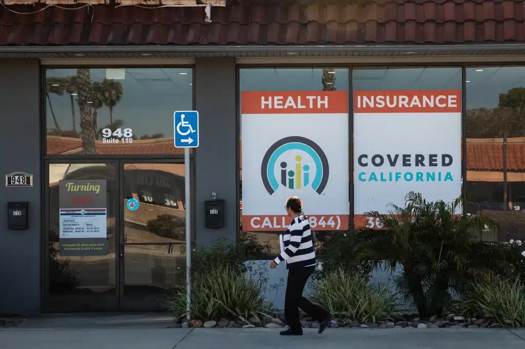 Woman walks past office window with Covered California logo. 