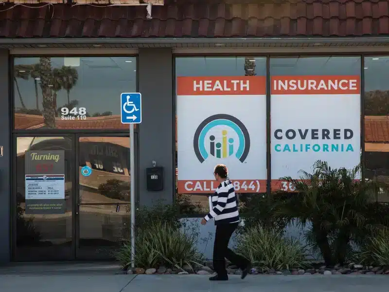 Woman walks past office window with Covered California logo.