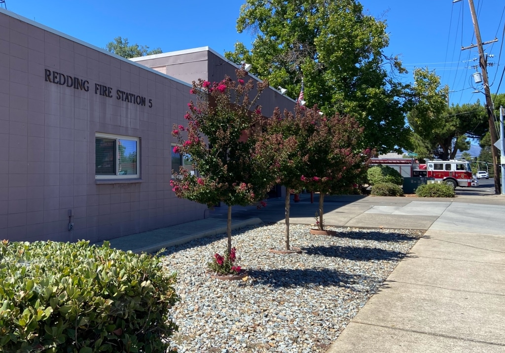 The painted brick Redding Fire Station 5 station, with pink blooming trees in front of it, and a fire truck pulling out in the background.
