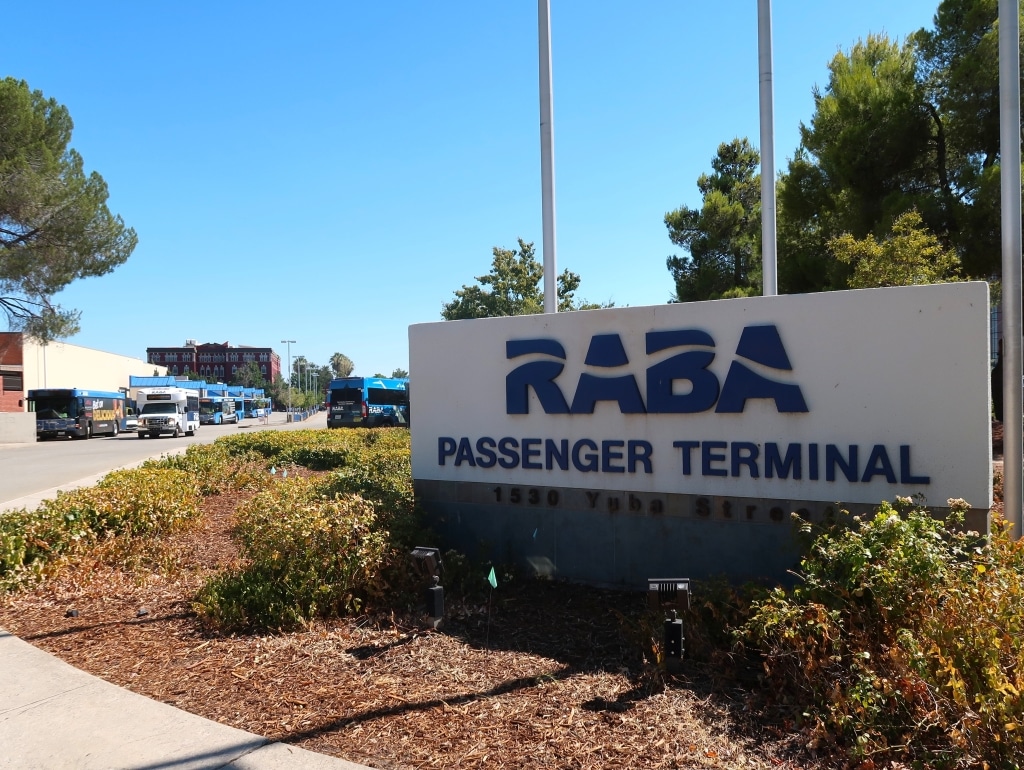 A sign reading "RABA Passenger Terminal" is in the foreground, with several blue buses and transit vehicles in the background.